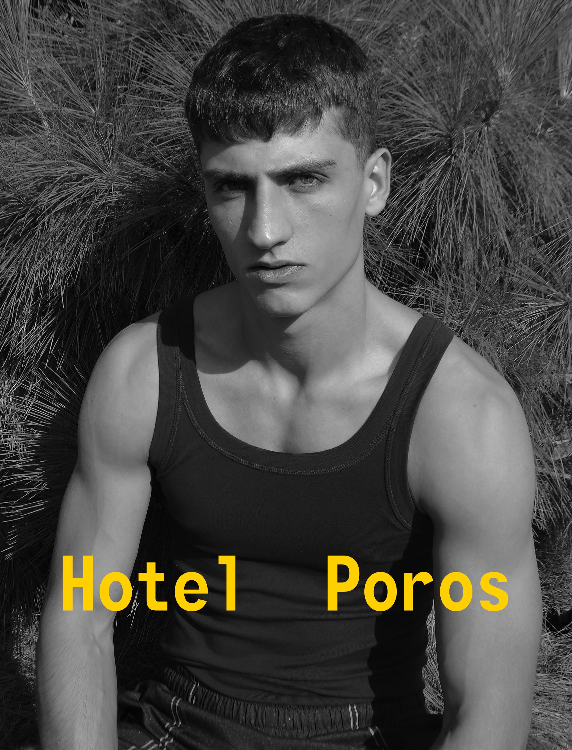 Man wearing a black tank top with 'Hotel Poros' text in yellow against a natural background